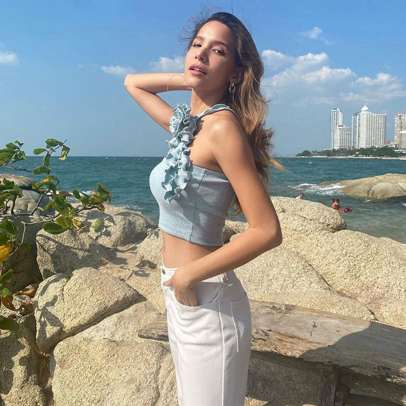 A woman poses with her hand on her head, wearing a light blue strapless top with floral details and white flared pants.