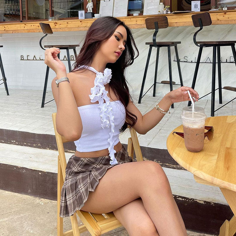 A woman in a white tube top and plaid skirt sits at a table with a drink.