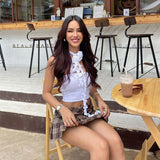 A woman in a white tube top and plaid skirt smiles at the camera while sitting at a table.