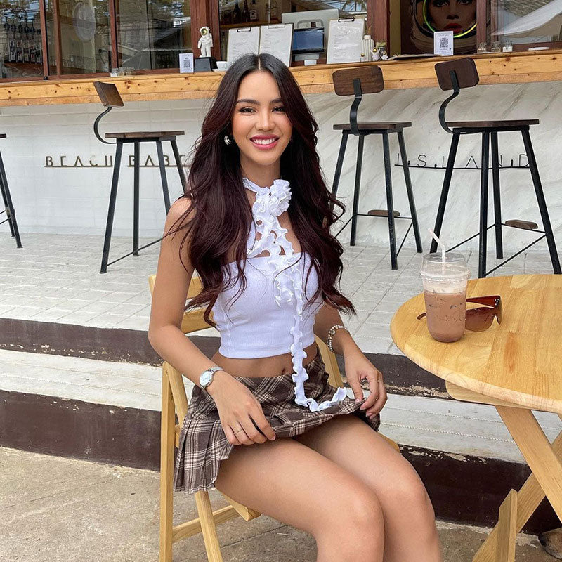 A woman in a white tube top and plaid skirt smiles at the camera while sitting at a table.