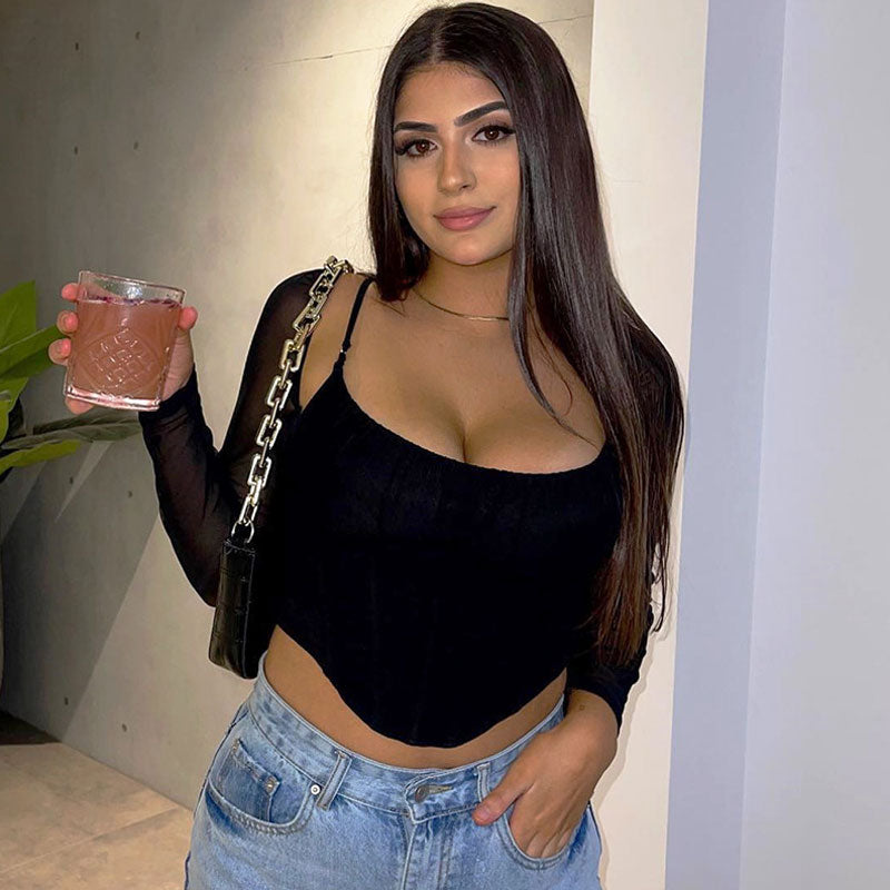 Woman in a black mesh long-sleeve corset top and blue jeans holding a drink.