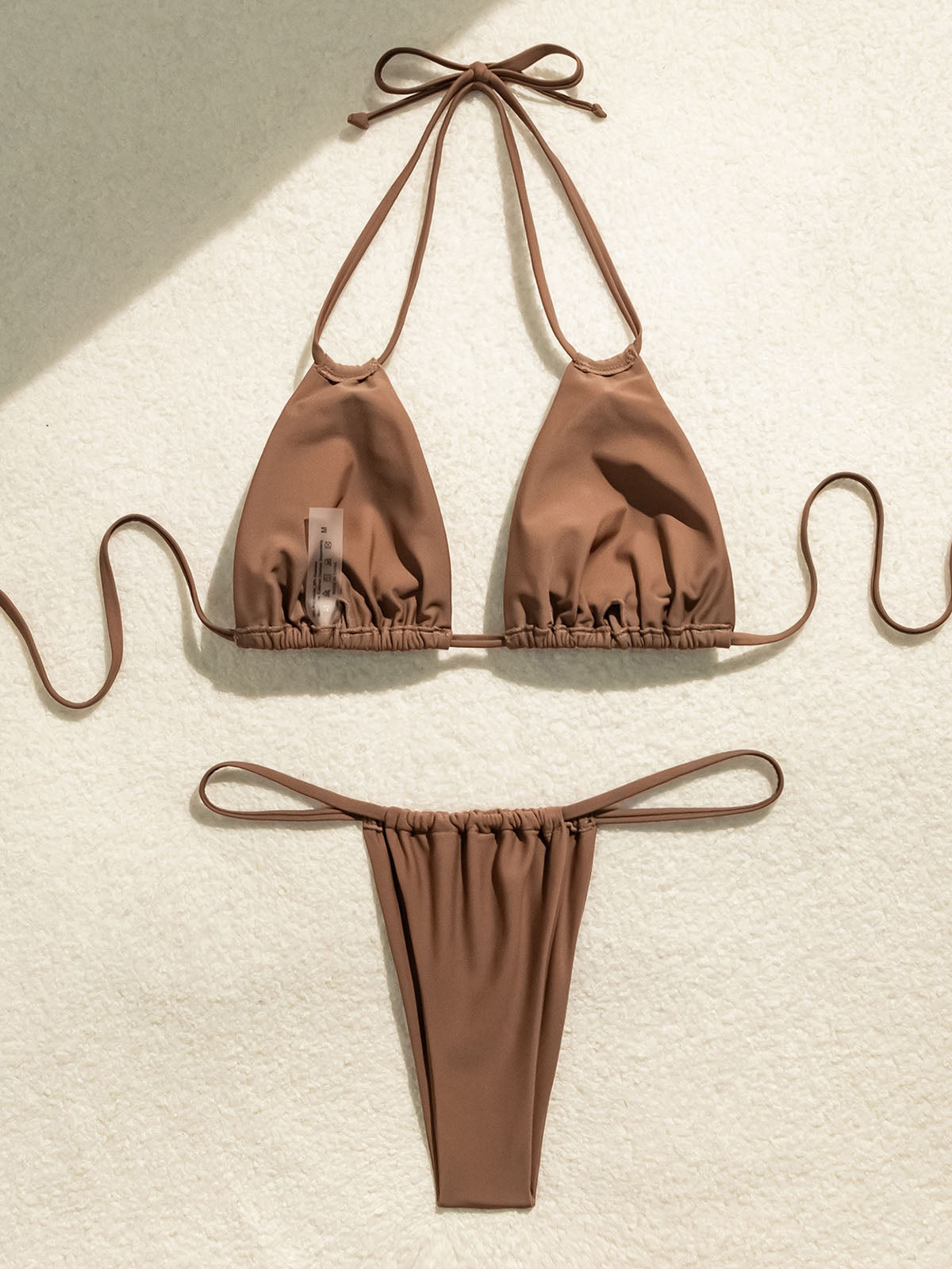Brown bikini laid out flat on a textured surface with a tag visible.
