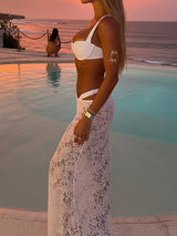 Side view of a woman in a white bikini and white lace maxi skirt by a pool