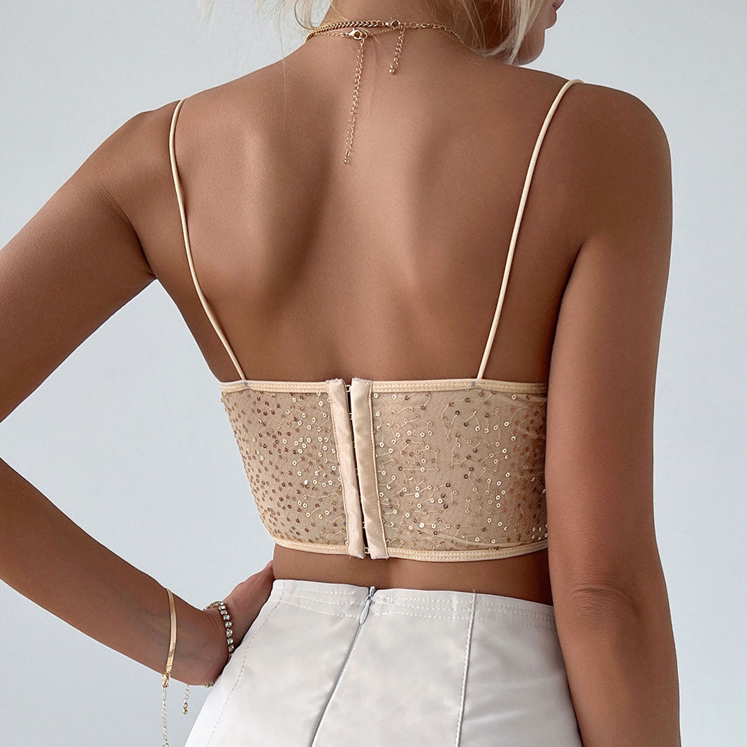 Back view of a woman wearing a beige sequined corset top with spaghetti straps and a zipper closure, paired with a white skirt.