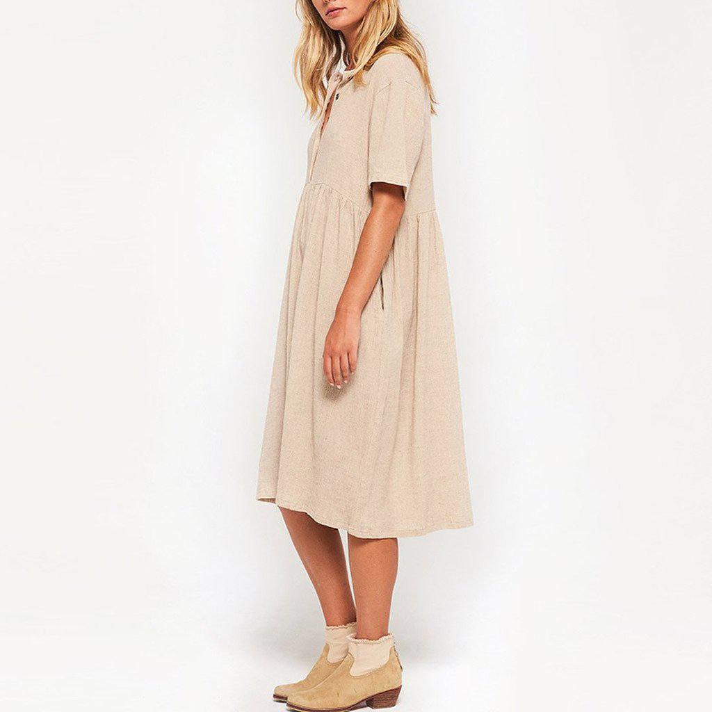 Woman standing in a beige linen dress and tan ankle boots