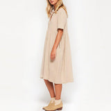 Woman standing in a beige linen dress and tan ankle boots