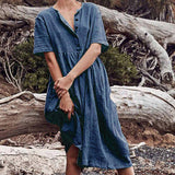 Woman standing against a log wearing a blue linen dress