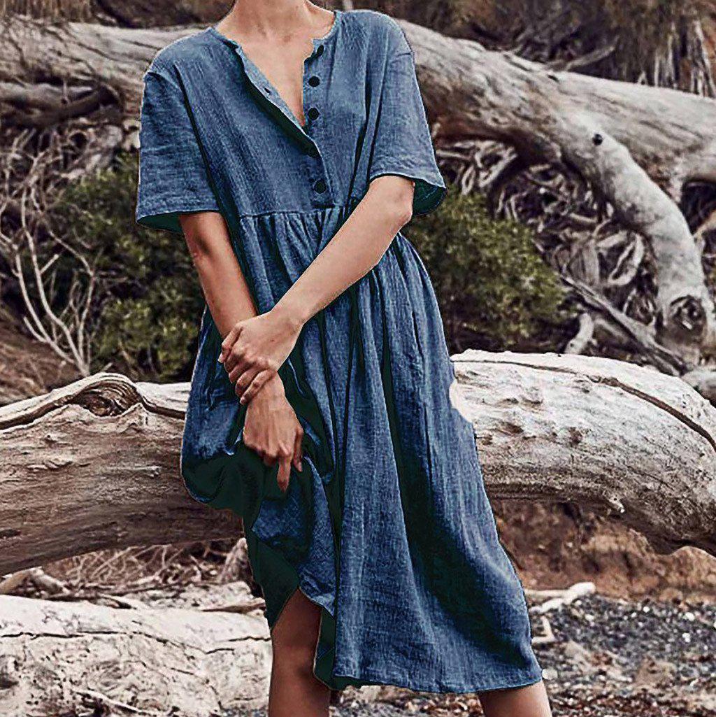 Woman standing against a log wearing a blue linen dress