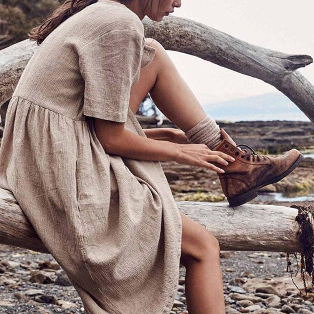Woman sitting on a log wearing a beige linen dress and brown boots