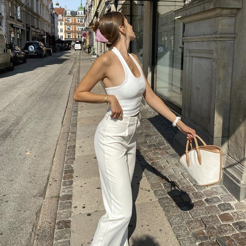 Woman in a white halter top and cream wide-leg pants, holding a white tote bag with tan accents.