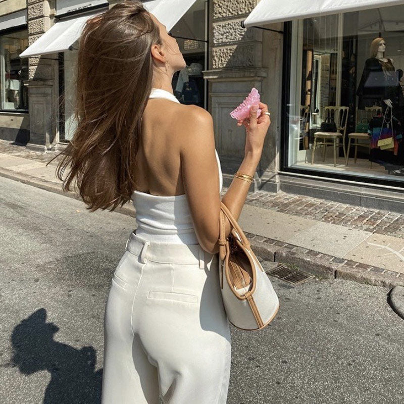 Woman from behind wearing a white halter top and cream wide-leg pants, holding a pink scrunchie.