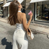 Woman from behind wearing a white halter top and cream wide-leg pants, holding a pink scrunchie.
