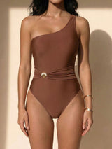 Woman wearing a one-shoulder brown swimsuit with a gold shell accent at the waist