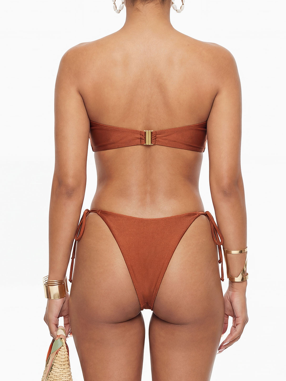 Back view of a woman wearing a brown strapless bikini with a gold clasp closure on the top, and tie-side bottoms.