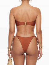 Back view of a woman wearing a brown strapless bikini with a gold clasp closure on the top, and tie-side bottoms.