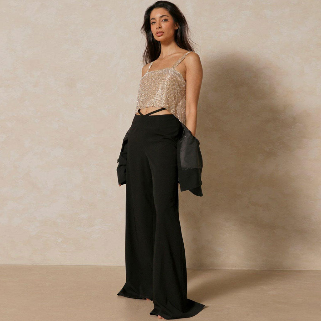 A woman in a gold sequined crop top and black wide-leg pants, with a black blazer draped over her shoulders.