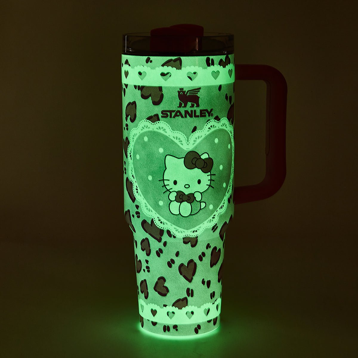 Glow-in-the-dark pink Stanley tumbler with Hello Kitty graphic and heart pattern in a dark setting