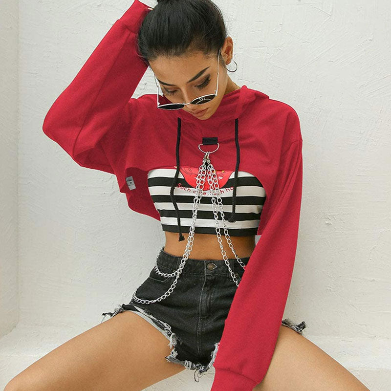 woman wearing a red cropped hoodie with chains over a striped crop top and denim shorts