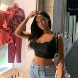 A young woman poses in front of a store window, wearing a black crop top and jeans.