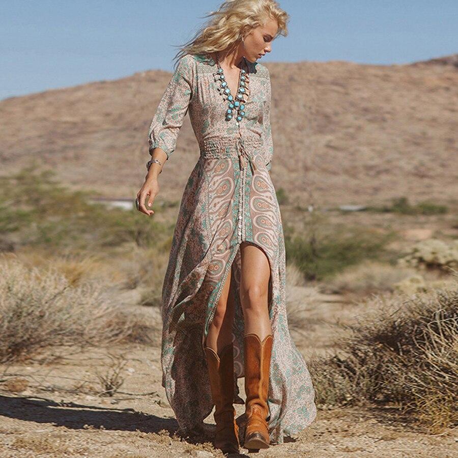 Woman walking in a desert wearing a flowy maxi dress with a paisley and floral print, brown cowboy boots, and a turquoise necklace.