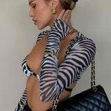 Close-up of a woman's profile, wearing a zebra print mesh top and gold earrings