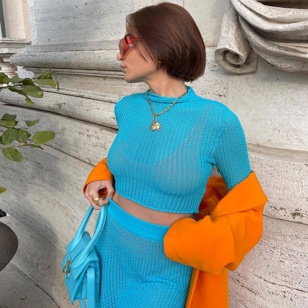 Close-up of a woman wearing a blue knit crop top and skirt with an orange blazer, showing off her accessories.