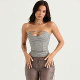 Woman wearing a gray strapless corset top with a cut-out detail and intricate silver lace-up accents, paired with brown lace-up pants.