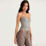 Side view of a woman in a gray strapless corset top with silver lace-up details, and brown lace-up pants.