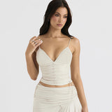 Model wearing a cream sleeveless V-neck top with ruched detailing and lace-up accents, paired with a matching skirt.