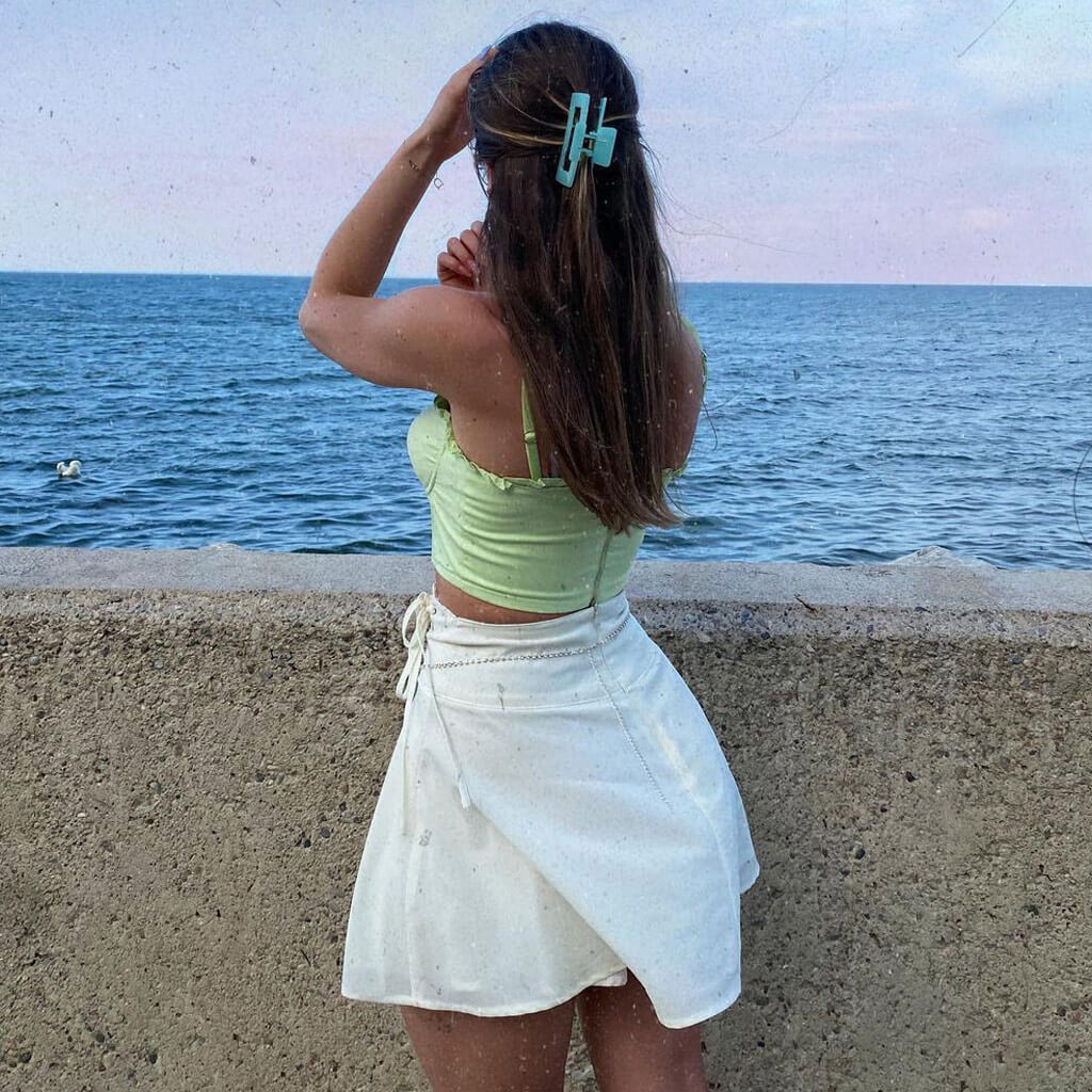 A woman in a lime green corset top and a white ruffled skirt looks out at the ocean.