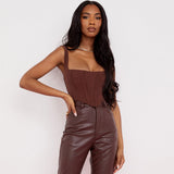 woman wearing a brown corset top and brown leather pants, posing with her hand on her hip