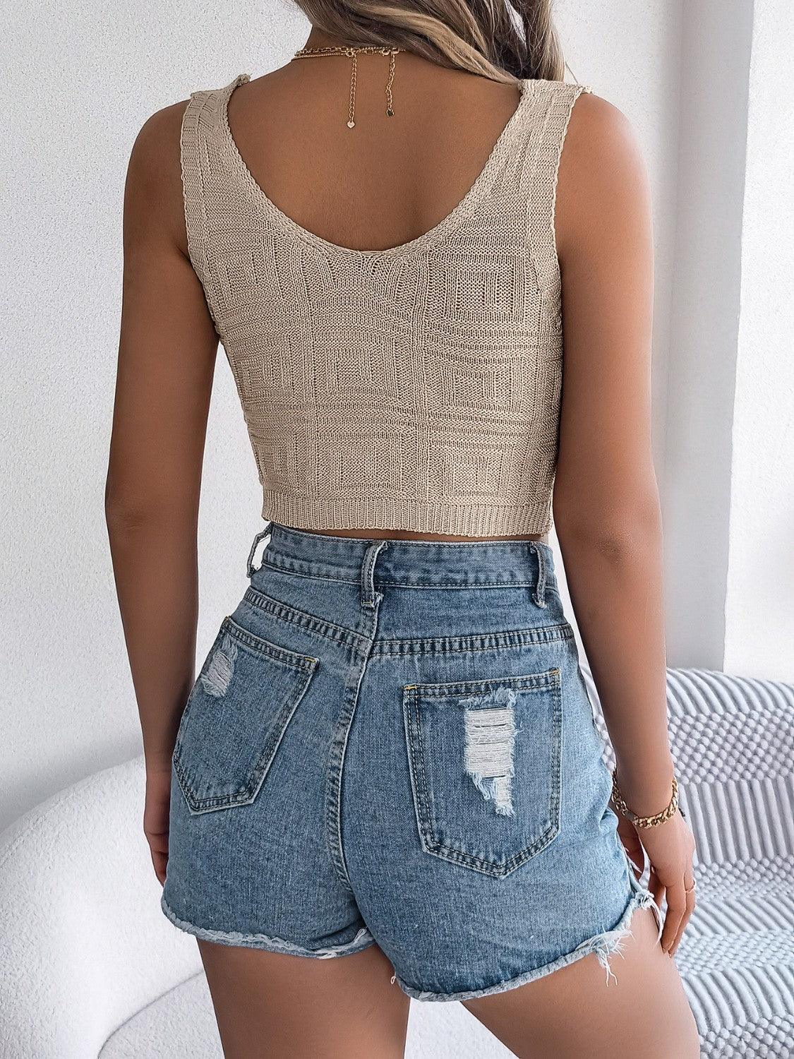 Woman wearing a beige knitted crop top and distressed denim shorts, back view
