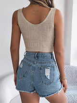 Woman wearing a beige knitted crop top and distressed denim shorts, back view