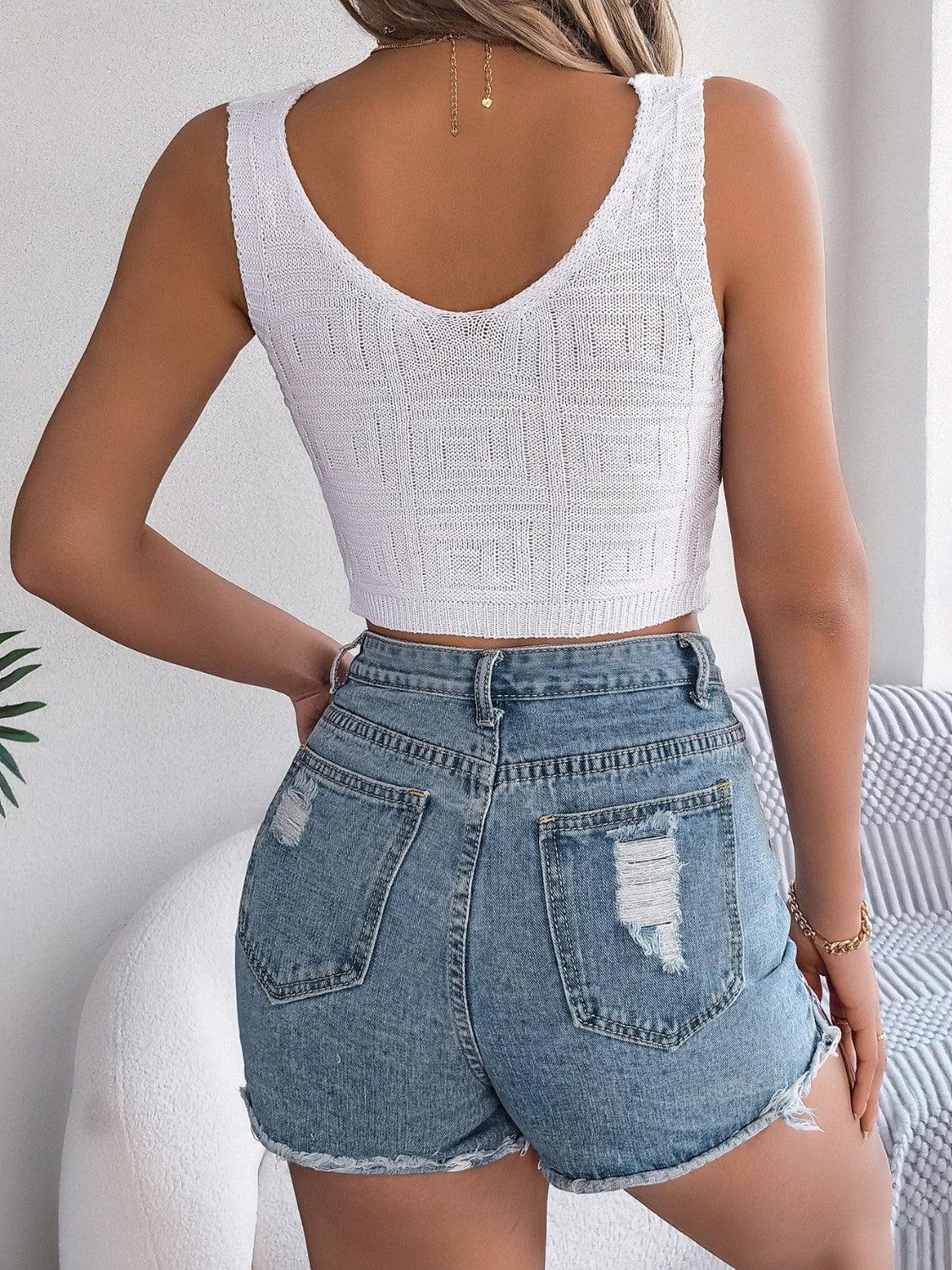 Woman wearing a white knitted crop top and distressed denim shorts, back view