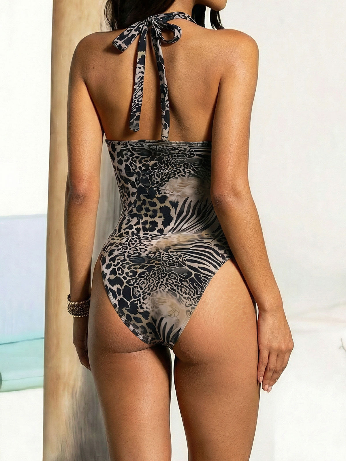 Back view of a woman wearing an animal print one-piece swimsuit with a halter tie.