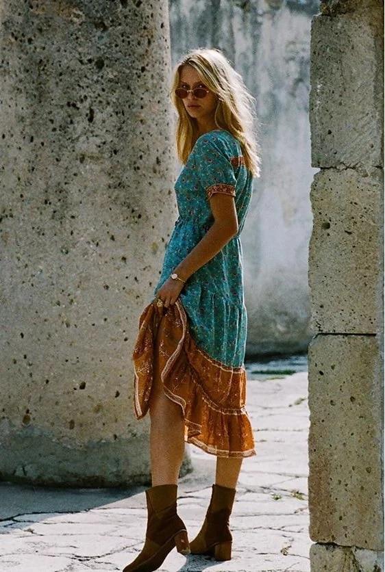 Side view of a woman wearing a teal floral midi dress with an orange hem panel, standing outdoors.