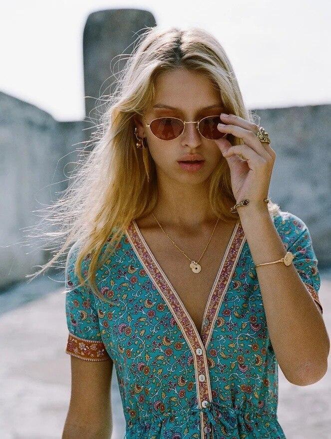 Close-up of a woman's face wearing a teal floral midi dress and sunglasses.