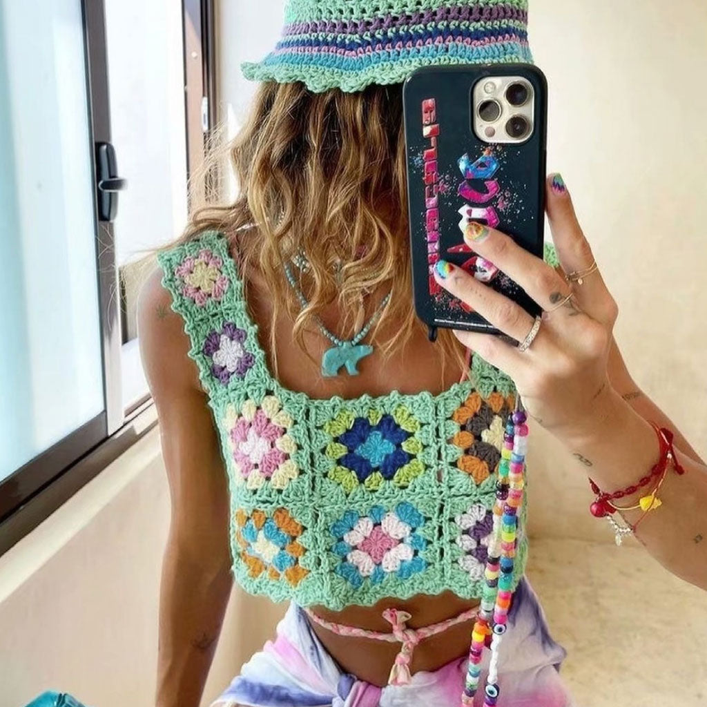 Woman taking a selfie in a mint green crochet crop top with colorful floral granny squares, wearing a matching bucket hat and colorful beaded necklaces.