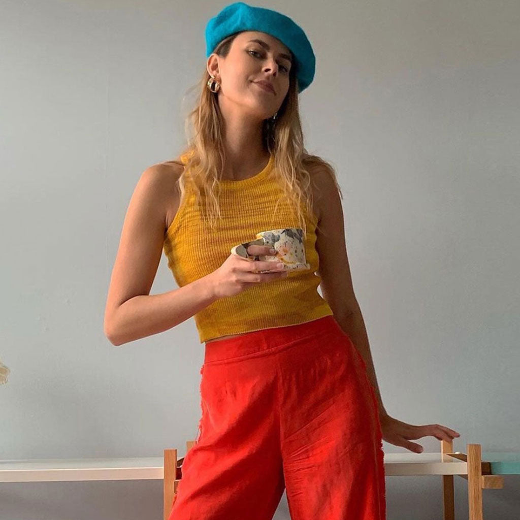 woman wearing a yellow ribbed crop top, red pants, and a blue beret