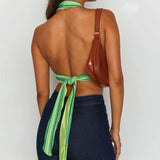 Back view of a woman wearing a green and white striped halter crop top tied at the back, with dark blue jeans and a brown shoulder bag.