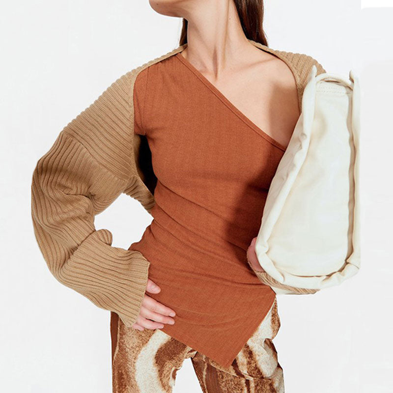 Woman wearing a rust-colored asymmetrical top and a tan shrug
