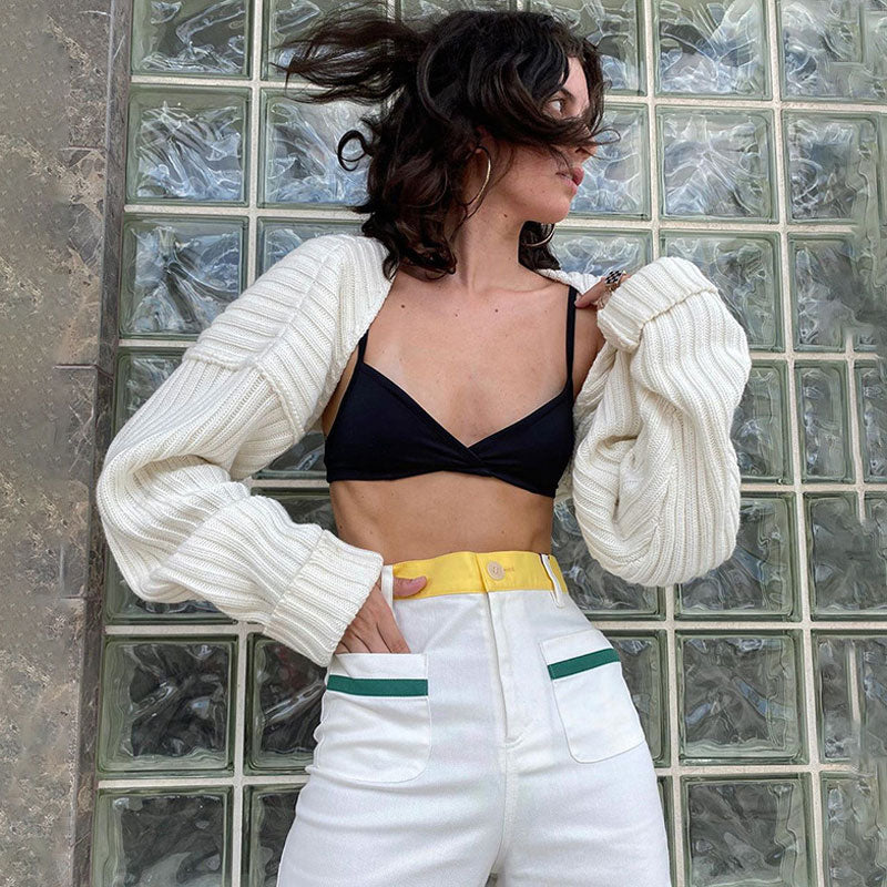 Woman wearing a white cropped shrug over a black bikini top and white pants with yellow and green accents.