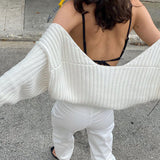 Woman wearing a white cropped shrug over a black bra and white pants.