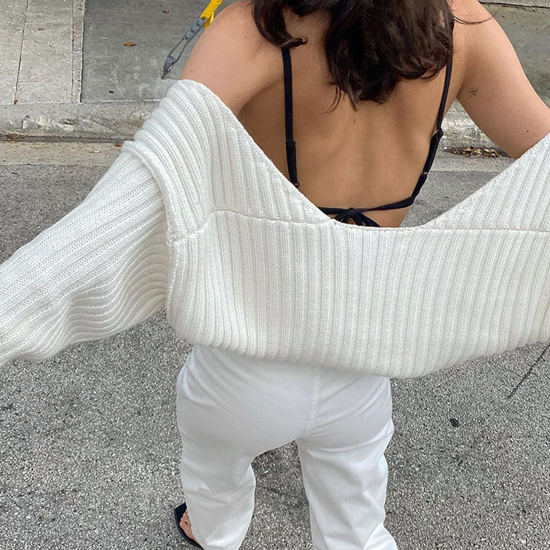 Woman wearing a white cropped shrug over a black bra and white pants.