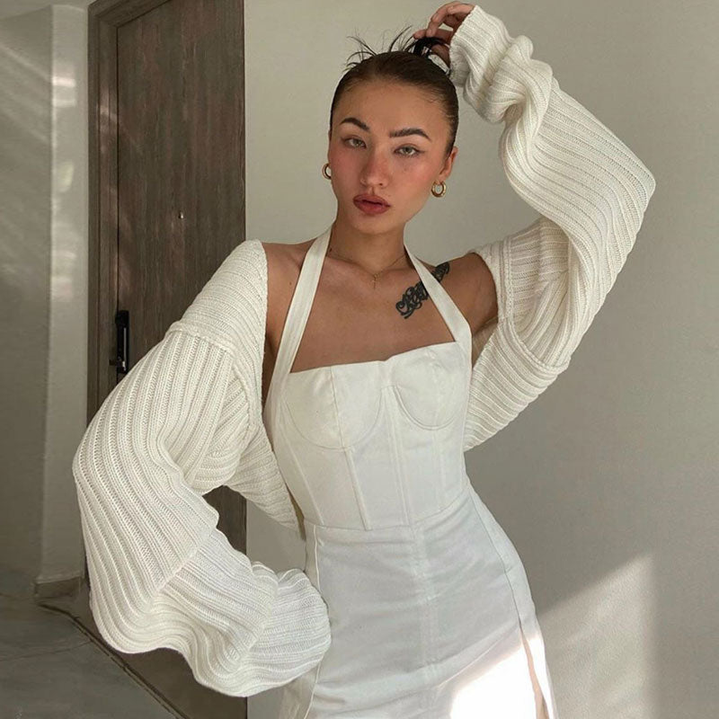Woman wearing a white cropped shrug over a white halter top and white dress.
