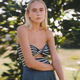 Woman wearing a blue and white striped strapless top with a cut-out detail and grey pants.