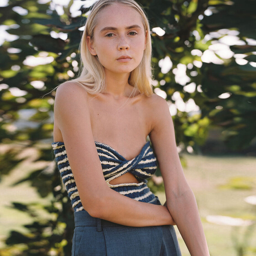 Woman wearing a blue and white striped strapless top with a cut-out detail and grey pants.