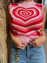 A young woman wearing a pink and red striped heart pattern cropped knit top, blue jeans, and sunglasses.